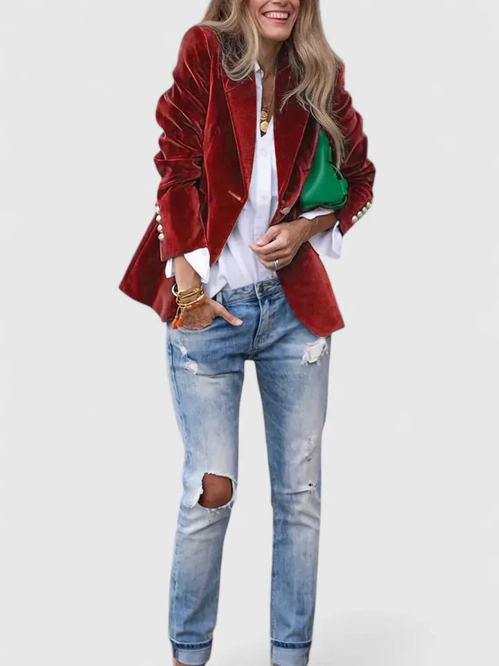 Blazer entallado rojo llevado abierto sobre una camisa blanca, combinado con vaqueros desgastados y bolso verde.
