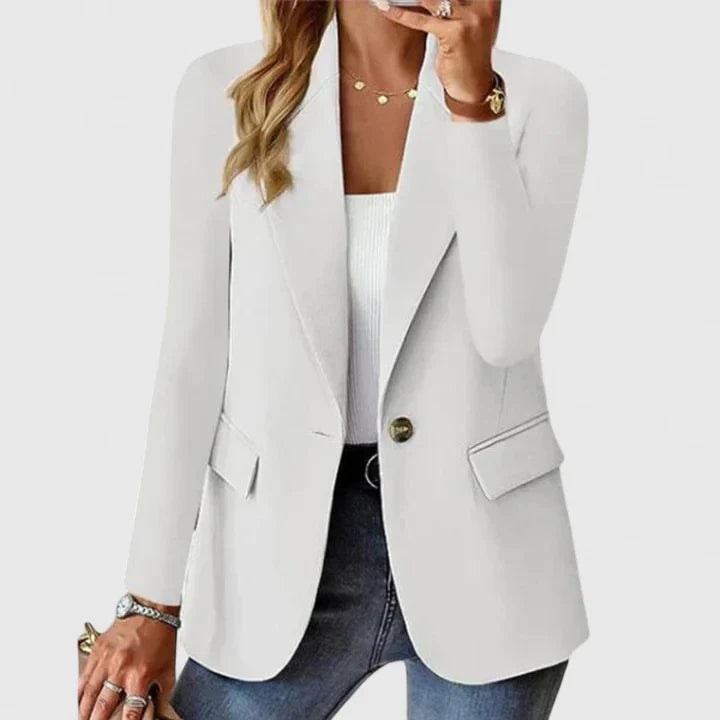 Blazer entallado blanco de un botón, con línea frontal definida, solapas y bolsillos con solapa, llevado sobre una camiseta blanca y vaqueros.