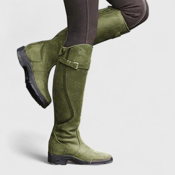 Bota alta verde oliva en vista lateral, con hebilla ajustable, paneles cosidos y tacón bajo.
