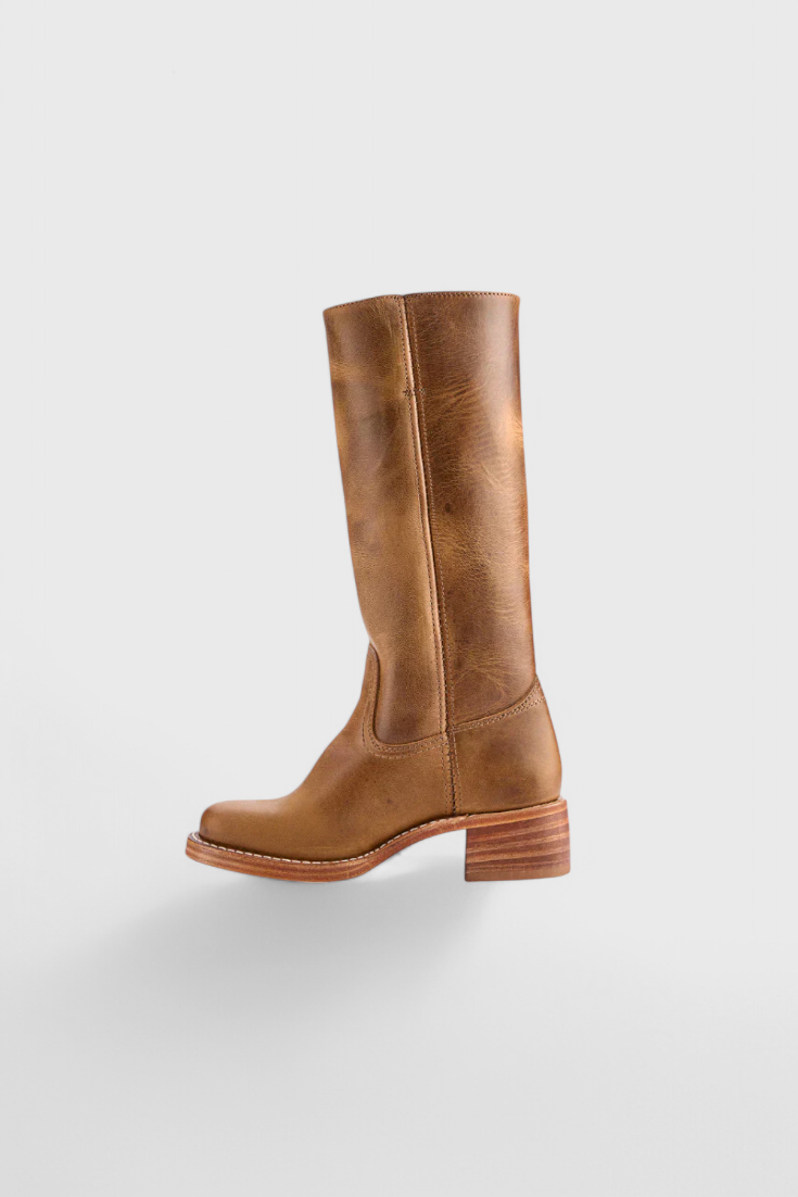 Bota alta marrón claro aislada en perfil, con silueta estilizada, puntera redondeada y tacón bajo.