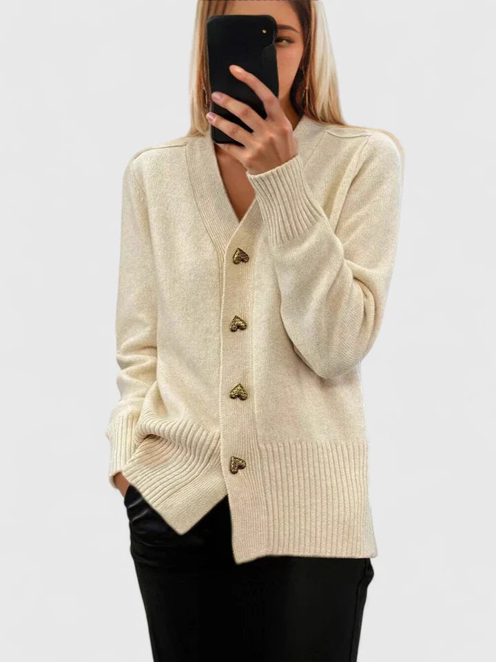 Cárdigan beige claro de corte relajado, cuello en V, botones de corazón y bajo acanalado combinado con pantalón negro.