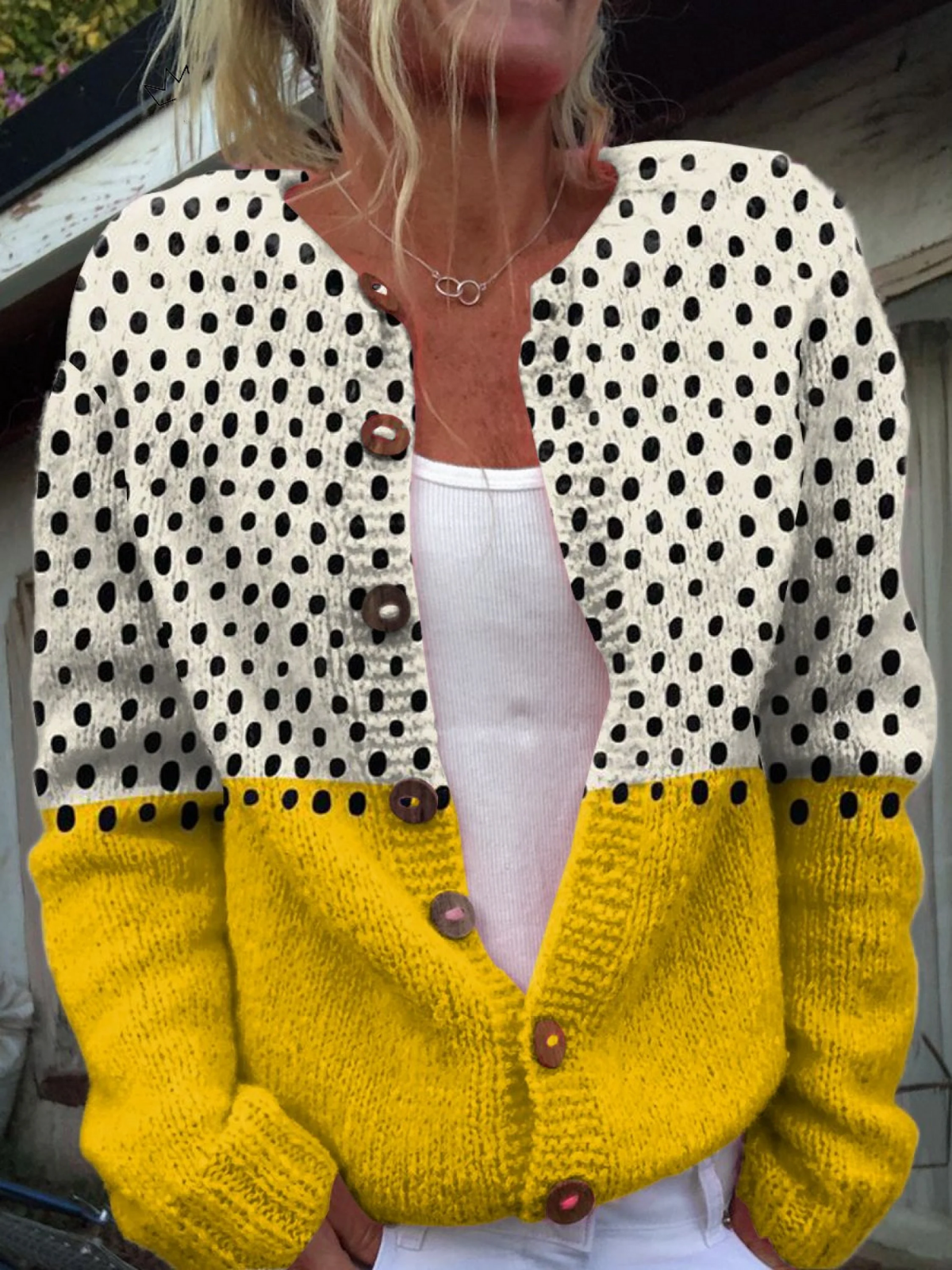 Cárdigan de escote en V con lunares oscuros en la parte superior, bloque amarillo en la parte inferior, botones frontales y bolsillos laterales; se lleva abierto sobre una camiseta clara.