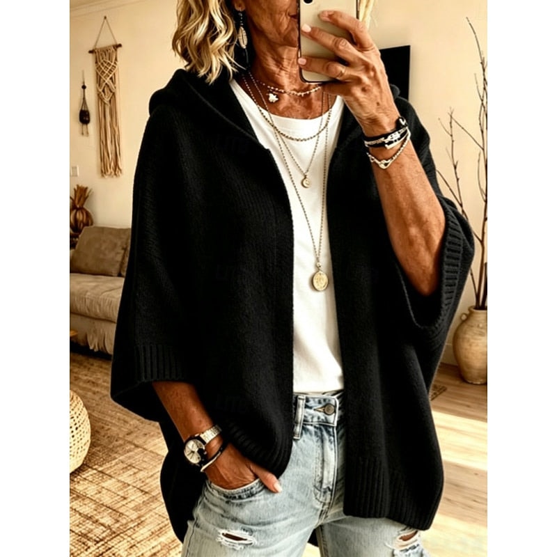 Cárdigan holgado negro con capucha y frente abierto, combinado con camiseta blanca y vaqueros claros.