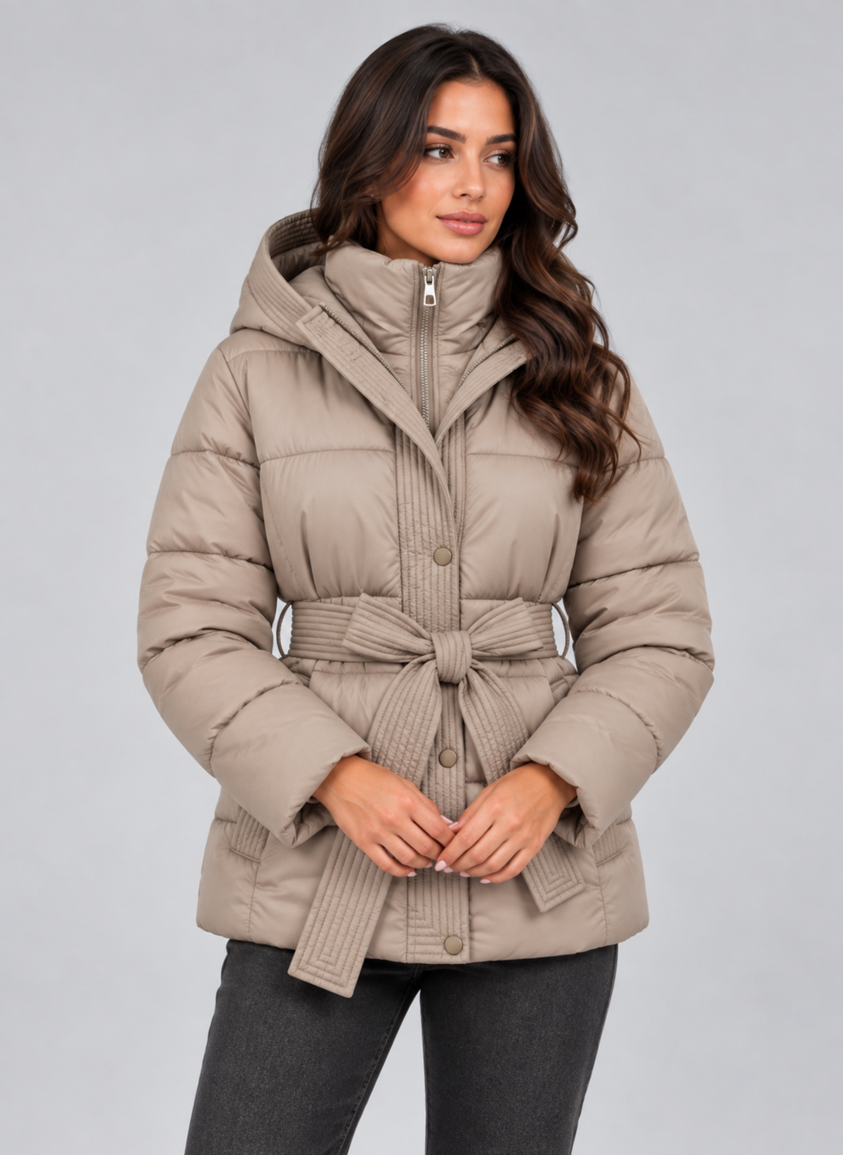 Chaqueta acolchada beige con capucha, cierre frontal y cinturón anudado, combinada con pantalones oscuros.