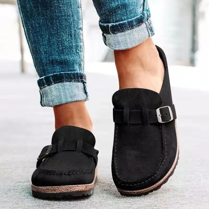 Mocasines planos negros con costuras marcadas, tira frontal y hebilla ajustable plateada.