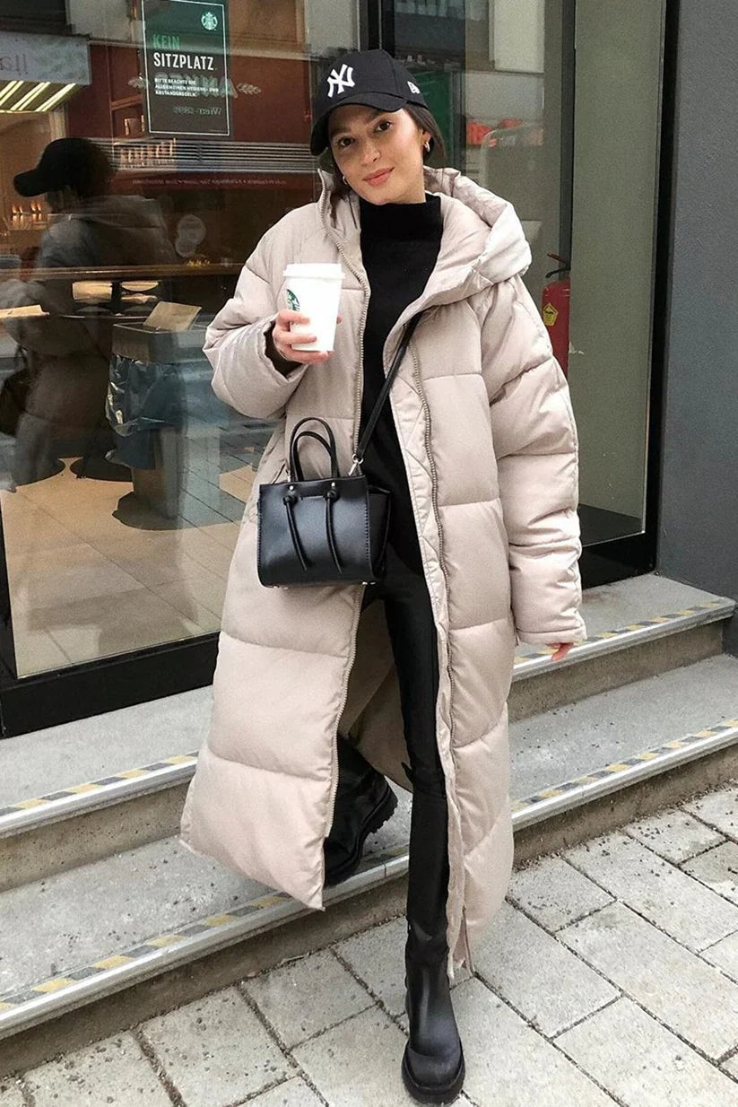 Abrigo acolchado largo en tono claro con capucha, mostrado abierto sobre un conjunto negro y botas altas.