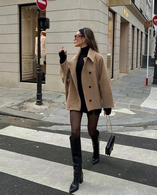 Abrigo corto recto en tono camel con cuello amplio y botones frontales, combinado con prendas negras en una calle urbana.