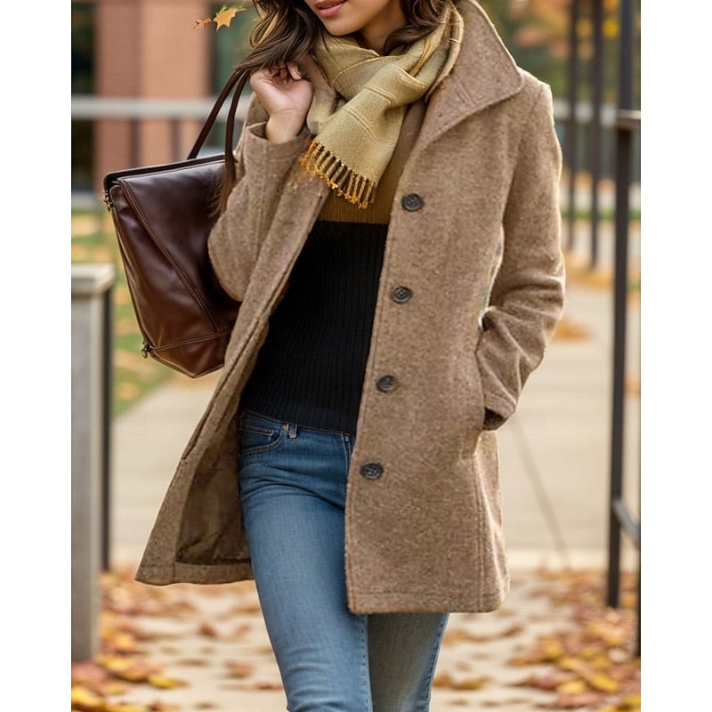 Abrigo entallado en tono beige con cuello de solapa y varios botones frontales, llevado sobre un conjunto informal en un entorno urbano.