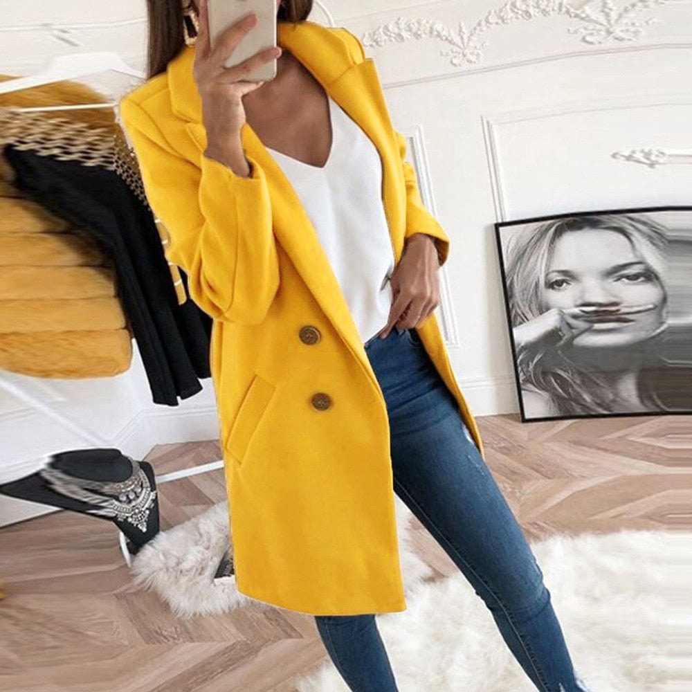 Abrigo amarillo de corte recto hasta medio muslo, con solapas, cierre frontal de dos botones y bolsillos laterales, combinado con camiseta blanca y vaqueros.