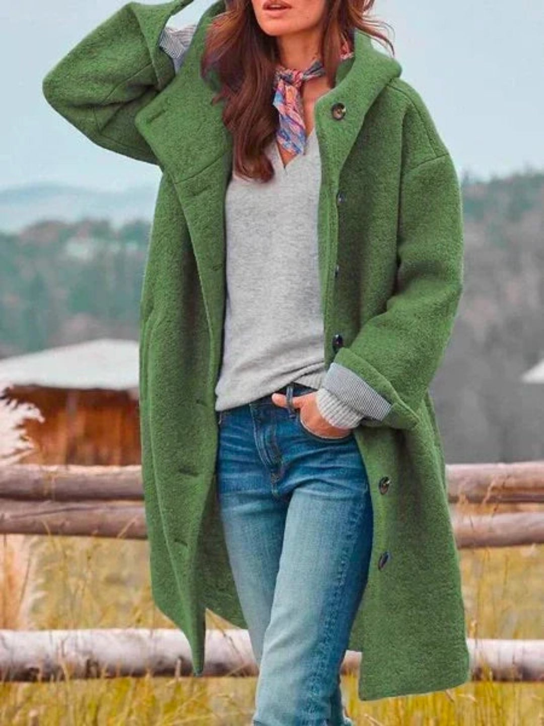 Abrigo largo verde con capucha y botones, mostrado de frente con las mangas remangadas y un bolsillo lateral.
