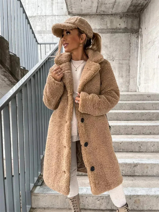 Abrigo teddy largo de corte recto en tono camel, con cuello amplio, botones frontales y bolsillos laterales, combinado con prendas claras.