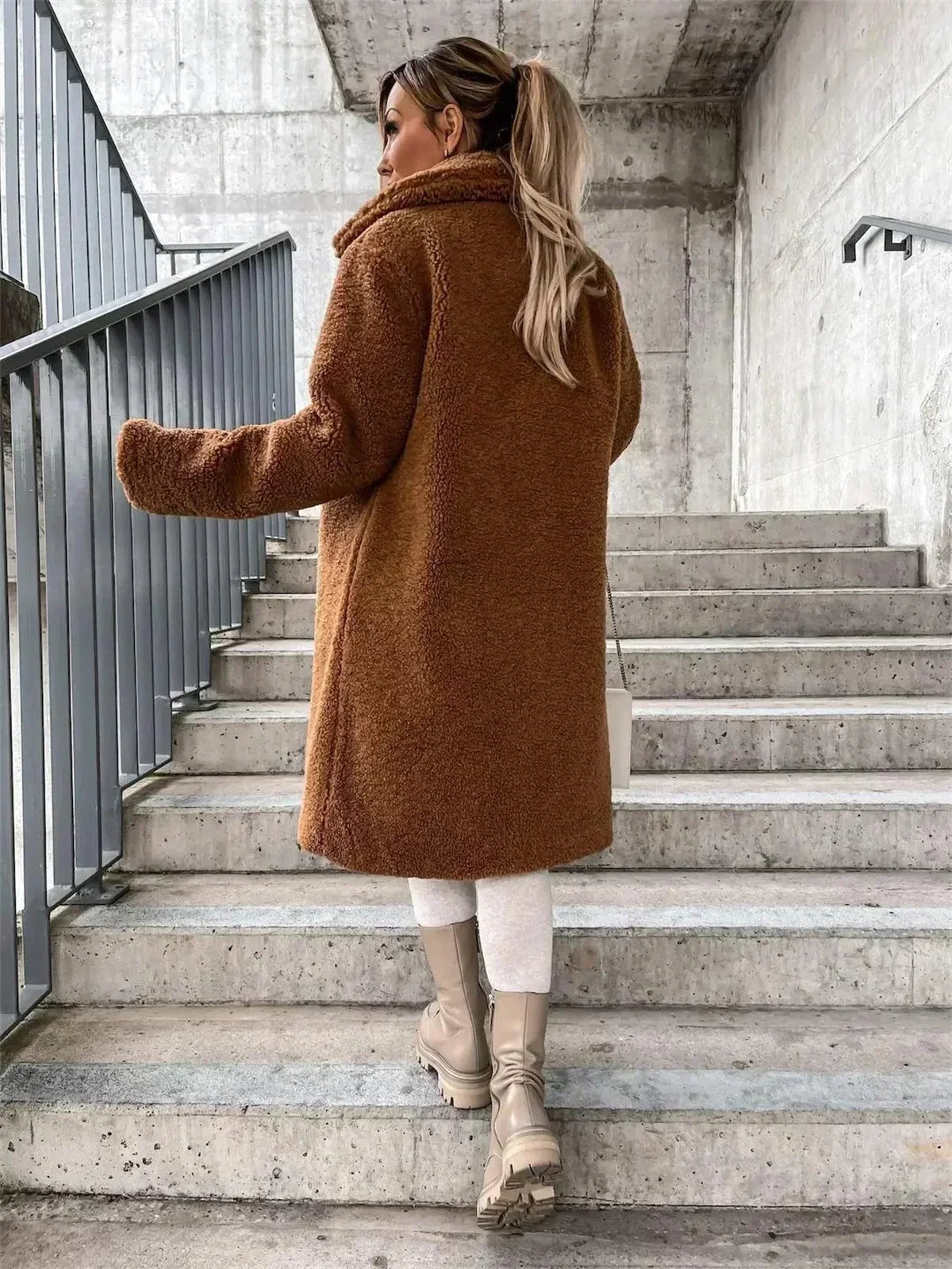 Vista posterior del abrigo teddy camel, donde se aprecia su corte largo y recto y el cuello elevado en la espalda.