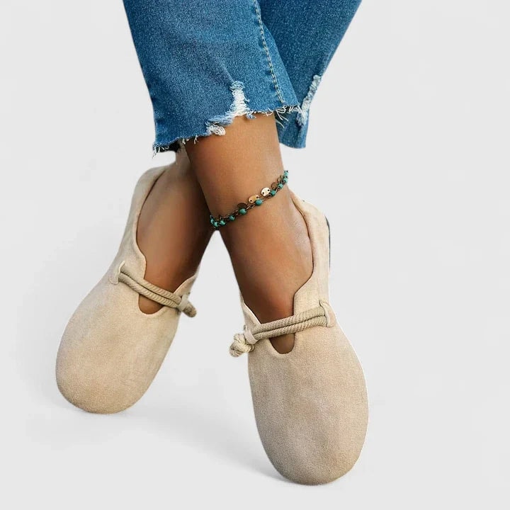 Bailarinas beige claro cruzadas en los pies, con sus tiras anudadas y aberturas visibles sobre el empeine.