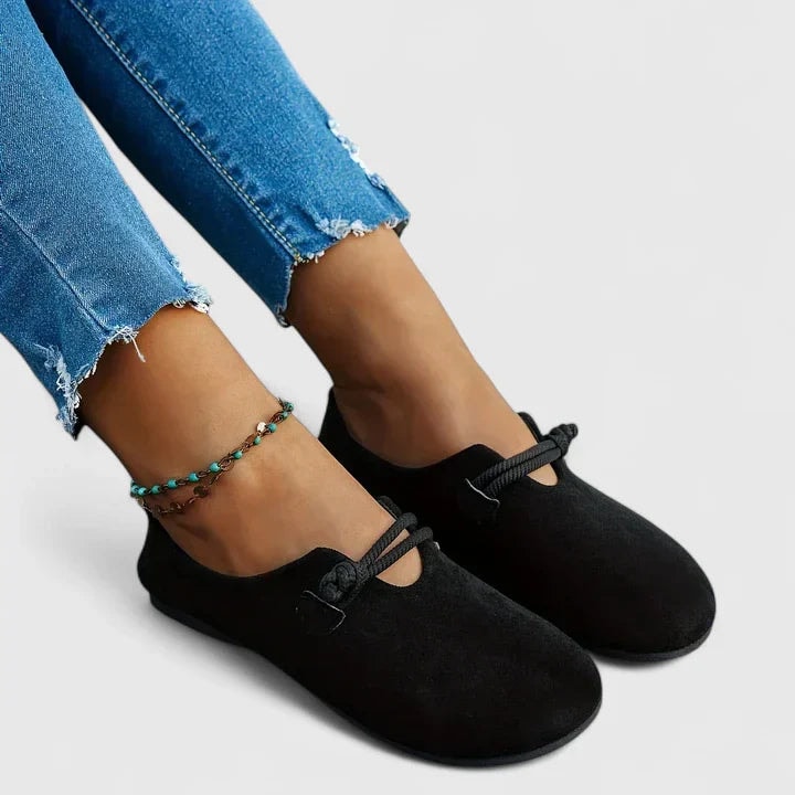 Bailarinas negras llevadas con vaqueros, mostradas en primer plano desde un ángulo lateral que resalta la punta redondeada y la tira de nudo.
