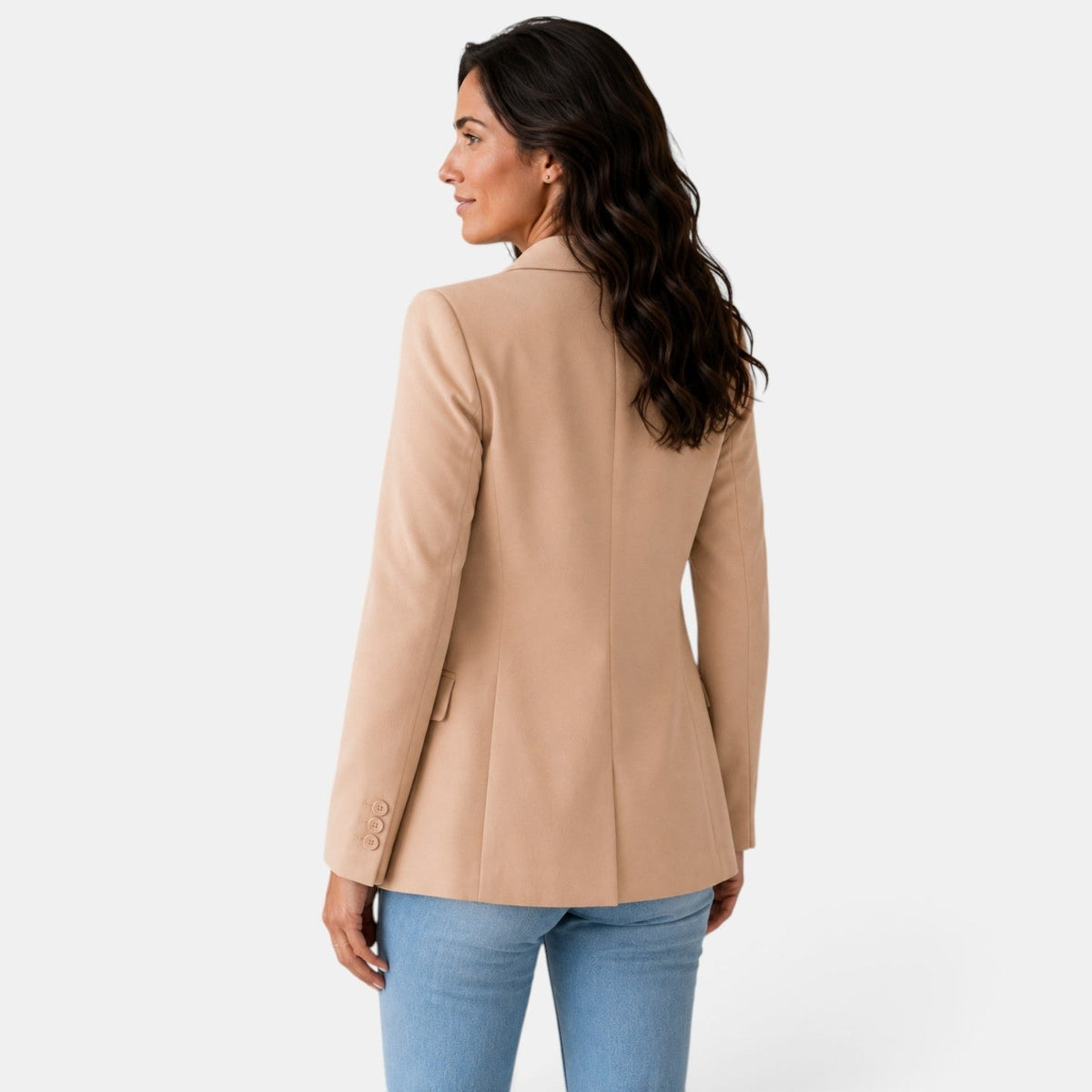 Vista posterior del blazer beige, con costura central, hombros definidos y corte entallado sobre los vaqueros.