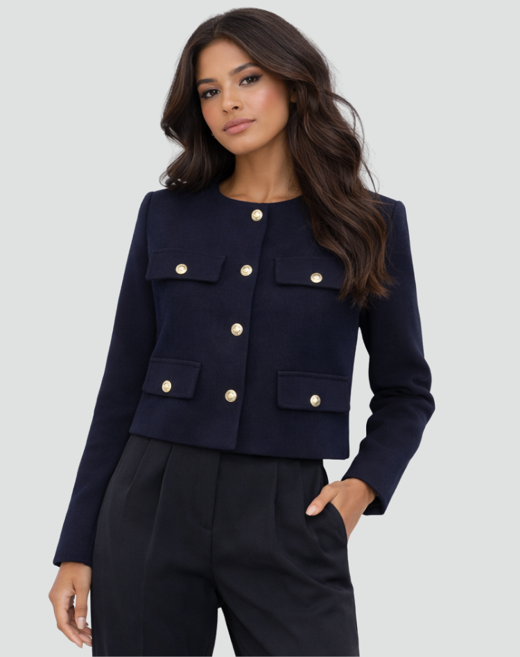 Blazer corto azul marino cerrado, con cuatro bolsillos decorativos y botones dorados sobre pantalón negro.
