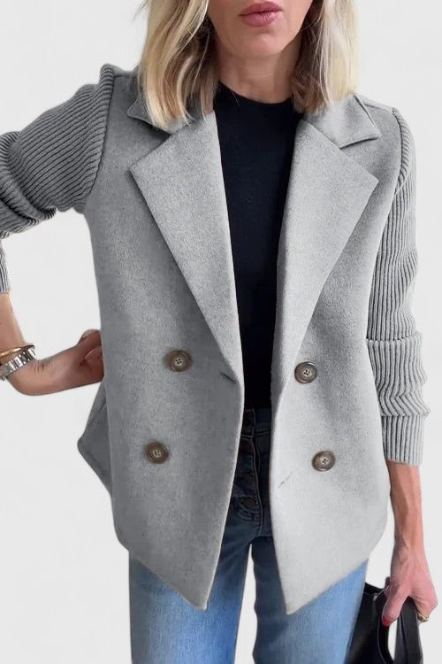 Blazer entallada gris claro con cierre de doble botonadura y mangas acanaladas, llevada sobre una camiseta negra.