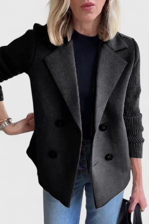 Blazer entallada negra de doble botonadura, con solapas clásicas y mangas acanaladas de textura marcada.
