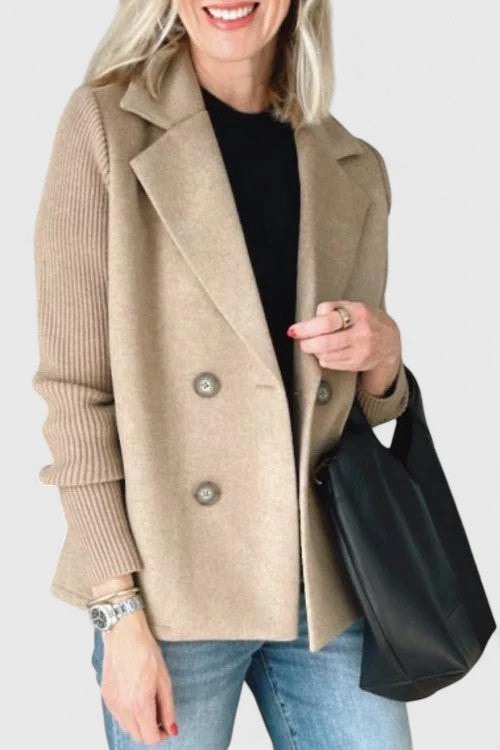 Blazer entallada beige con doble botonadura y mangas acanaladas, mostrada abierta sobre una camiseta negra y junto a un bolso negro.