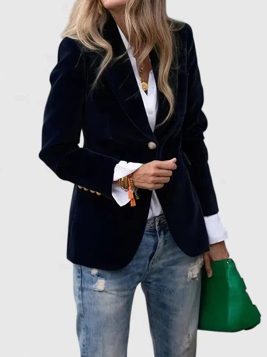 Blazer entallado azul marino de un botón con solapas, combinado con camisa blanca, vaqueros desgastados y bolso verde.