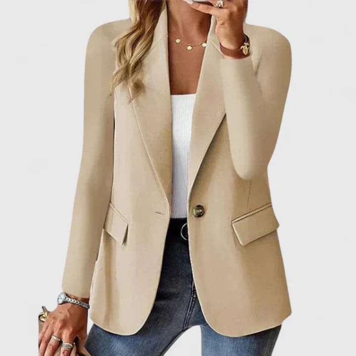 Blazer entallado beige claro de un botón, con mangas largas y solapas, sobre una camiseta blanca y vaqueros oscuros.