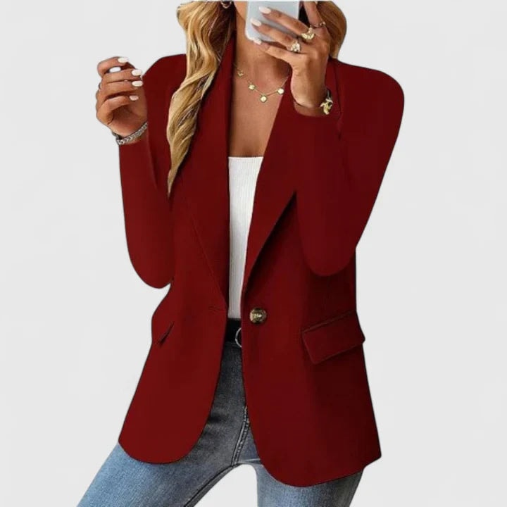 Blazer entallado burdeos de un botón, mostrado con las solapas abiertas y bolsillos con solapa, combinado con camiseta blanca y vaqueros.