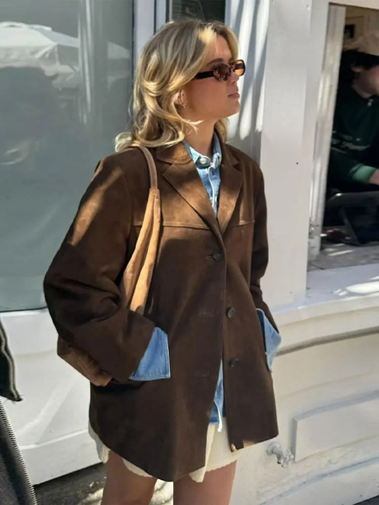 Vista de perfil del blazer marrón holgado con solapas, botones y bolsillos laterales, llevado con camisa vaquera y falda clara.