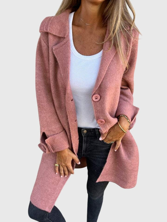 Blazer largo rosa con solapas amplias y botones, llevado abierto sobre una camiseta blanca y vaqueros oscuros.