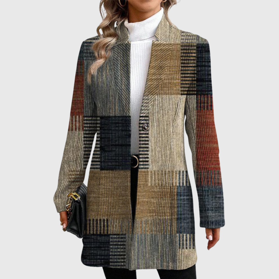 Blazer largo de cuadros patchwork en tonos gris, beige, marrón y negro, con corte estructurado, solapas y cierre frontal, combinado con jersey blanco de cuello alto.