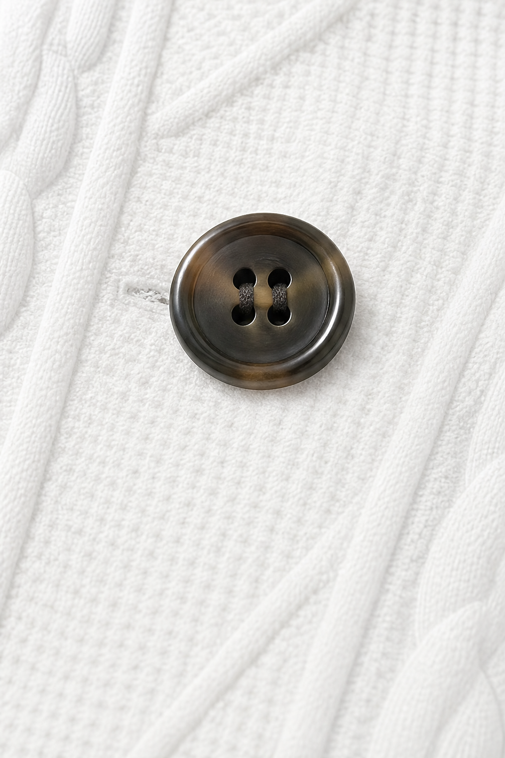 Detalle de un botón oscuro de cuatro orificios sobre la superficie texturizada del blazer.