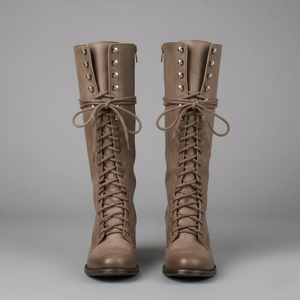 Par de botas altas beige de frente, con cordones cruzados desde la puntera hasta la caña y lazos laterales.
