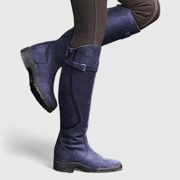 Bota alta azul en una pierna, destacando la hebilla lateral, las costuras y la suela negra.