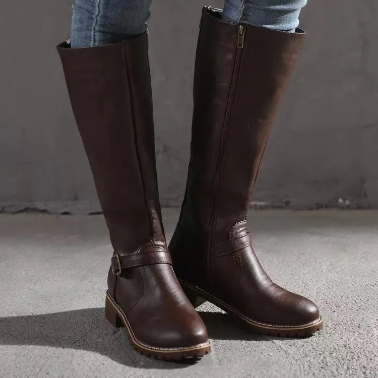 Par de botas altas marrón oscuro con cremallera lateral visible, correa con hebilla y tacón bajo.