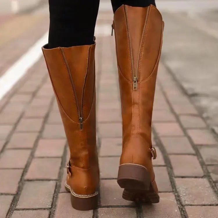 Parte posterior de botas altas marrón cobrizo con cremalleras largas y tacones bajos, caminando sobre una acera.