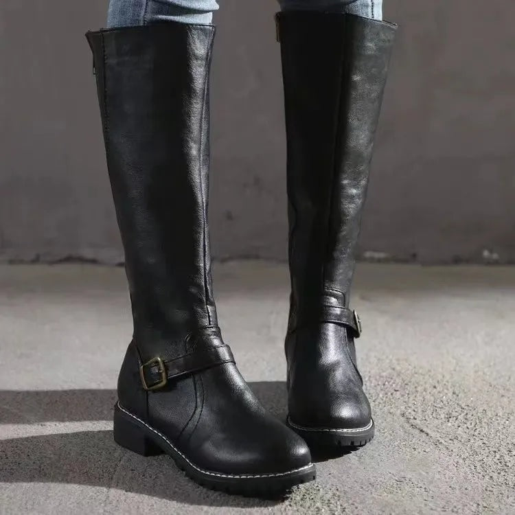 Botas altas negras de frente, con caña recta, hebillas laterales, tacón bajo y suela dentada.