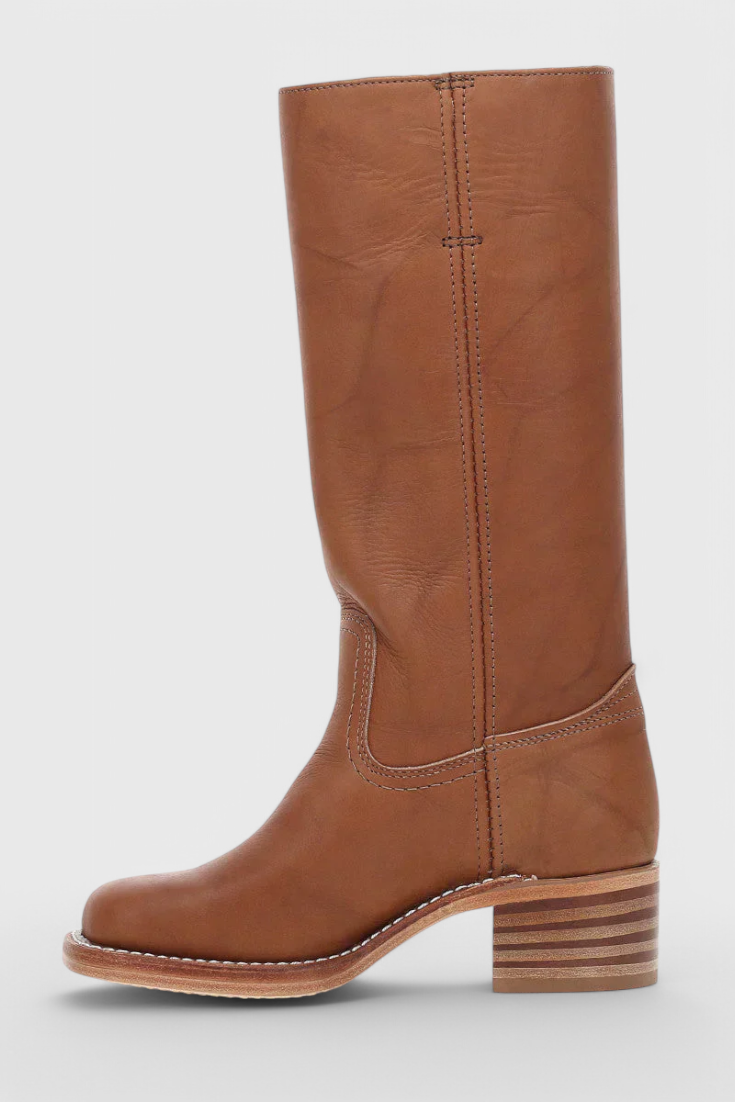 Bota alta marrón mostrada de perfil hacia el lado contrario, con costura trasera visible y tacón bajo estriado.