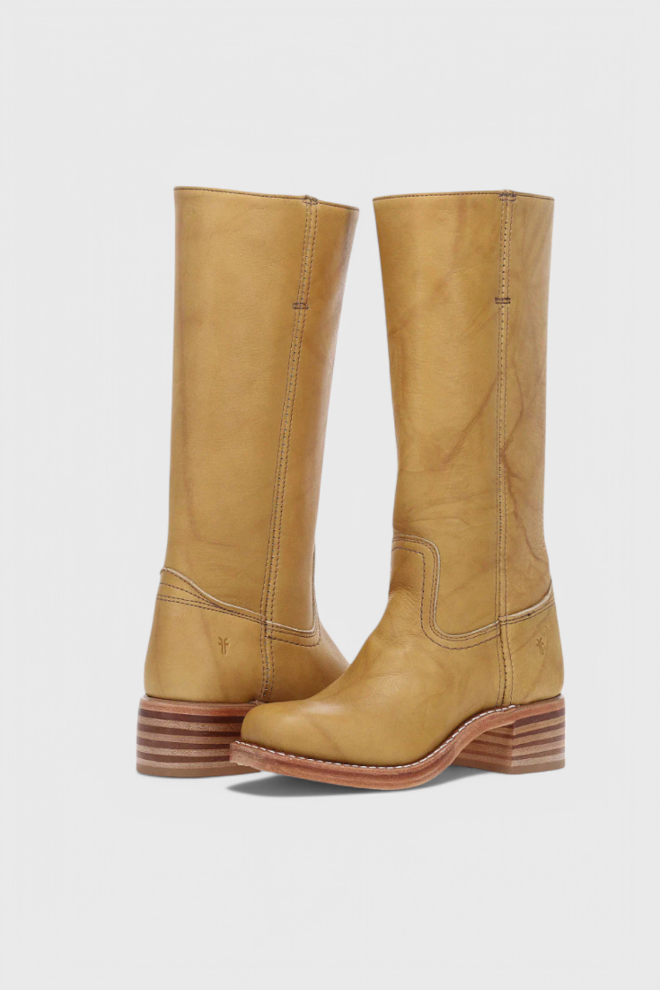 Dos botas altas color mostaza colocadas en ángulo, con costuras visibles y tacones bajos de varias capas.