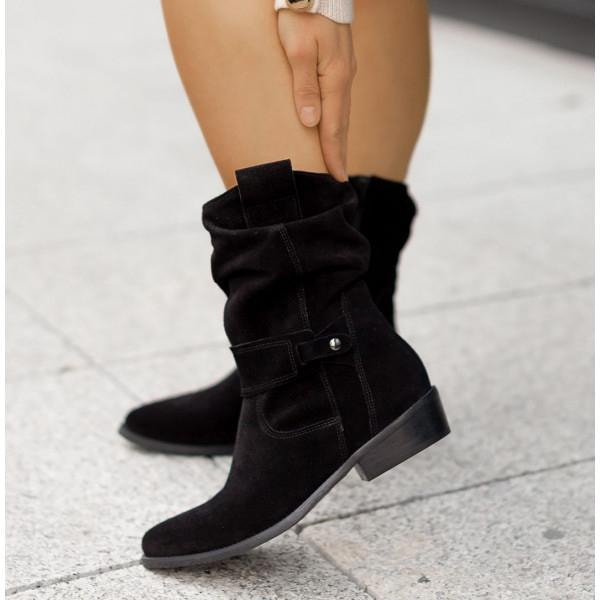 Botas negras de media caña con punta redondeada, caña fruncida y correa decorativa, mostradas sobre una superficie clara.