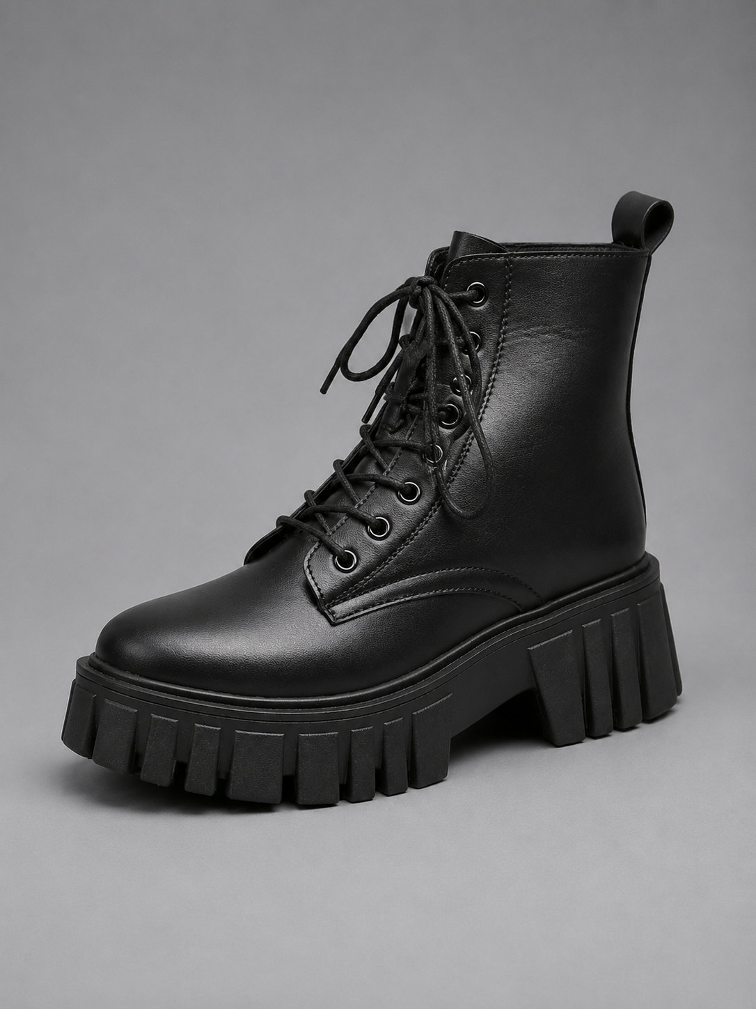 Bota militar negra de plataforma con cordones, vista en tres cuartos, con suela dentada de bloques marcados y tirador trasero.