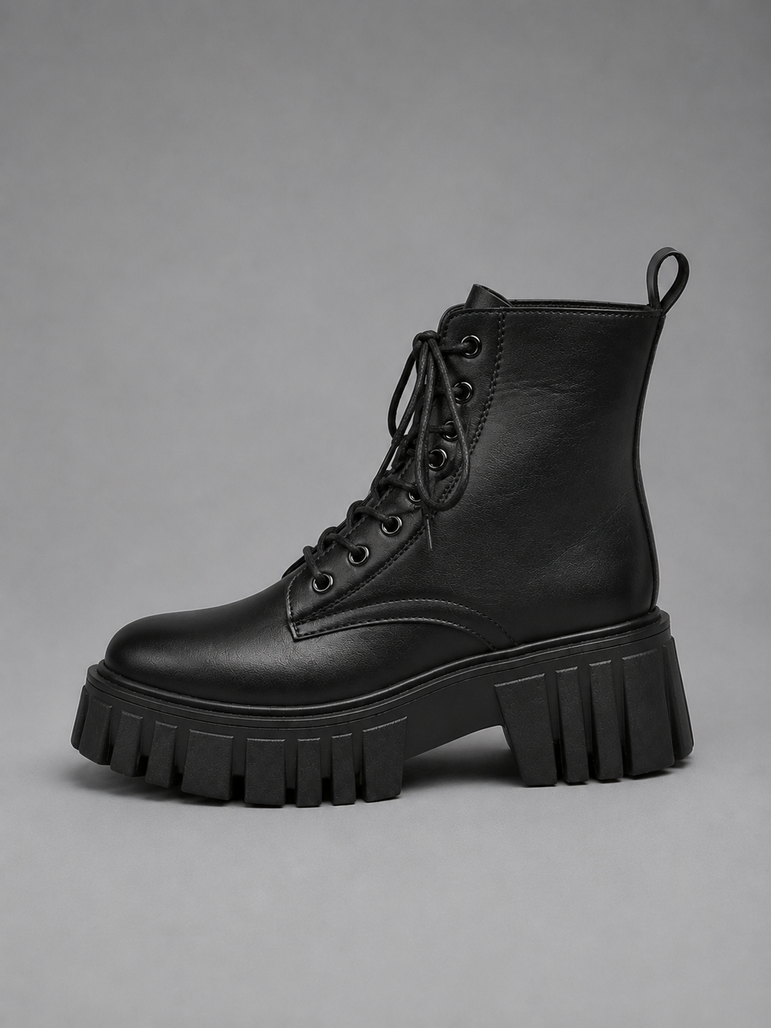 Bota negra de plataforma mostrada de perfil, con diseño al tobillo, cordones frontales y suela dentada prominente.