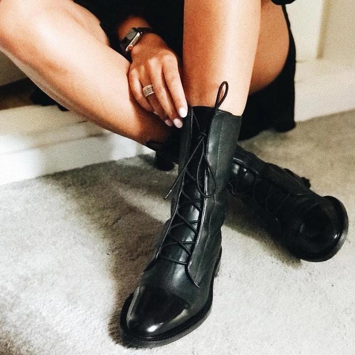 Persona ajustando los cordones de un botín negro mientras el otro permanece junto a su pierna.
