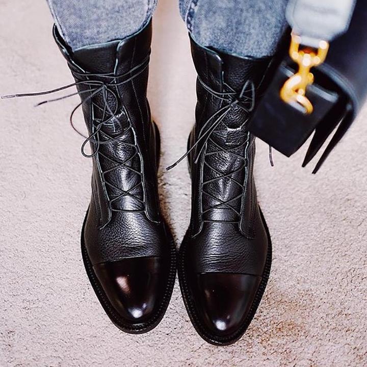 Botines negros de caña media combinados con vaqueros y un bolso negro, vistos desde arriba.