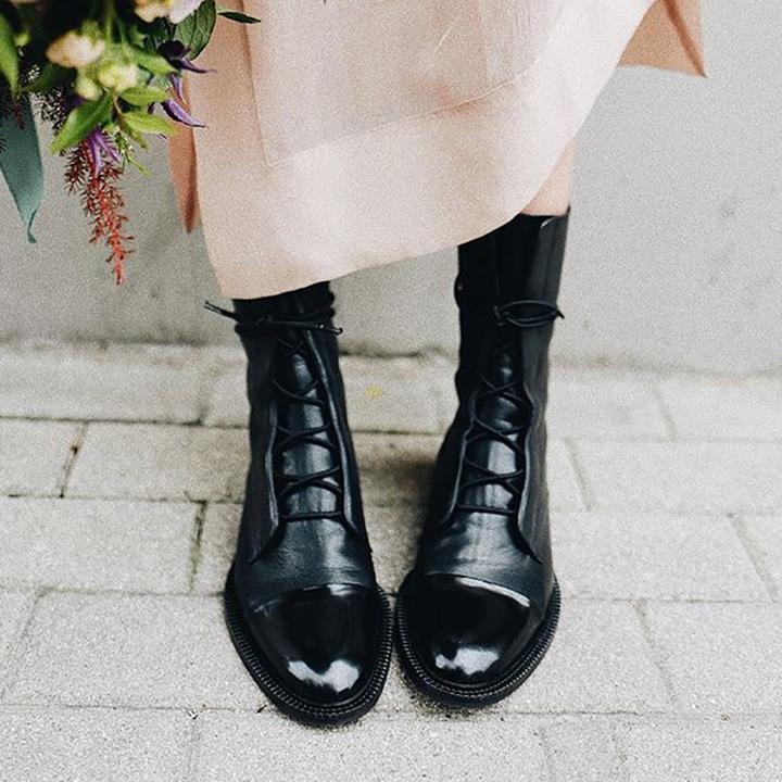 Botines negros con cordones llevados con un vestido claro, en una escena exterior sobre pavimento.