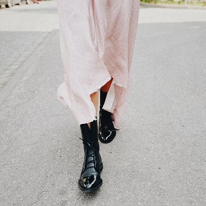 Una persona camina con botines negros de caña media y un vestido largo claro sobre una calle.