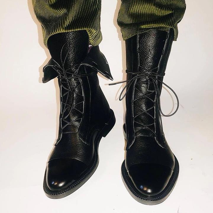 Botines negros de caña media con cordones, llevados con pantalones verdes recogidos, vistos de frente.