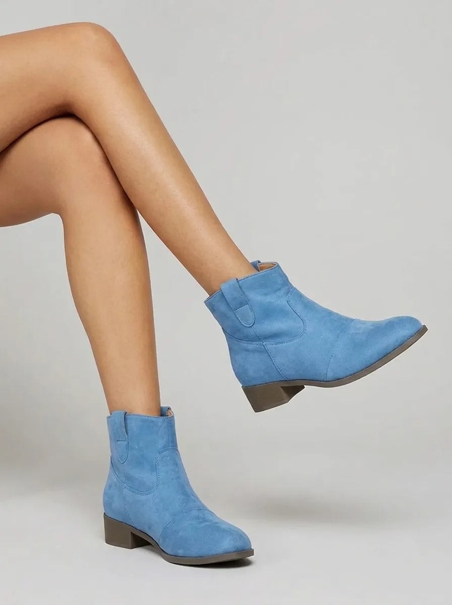 Botines Yolanda azules en movimiento, con un pie elevado para mostrar la silueta western y el tacón bajo.