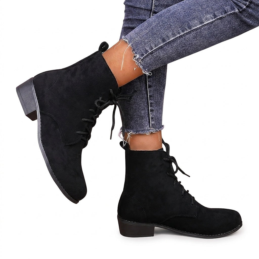 Botines negros de mujer con cordones, puntera redondeada y tacón bajo, mostrados en un conjunto sobre unos vaqueros.
