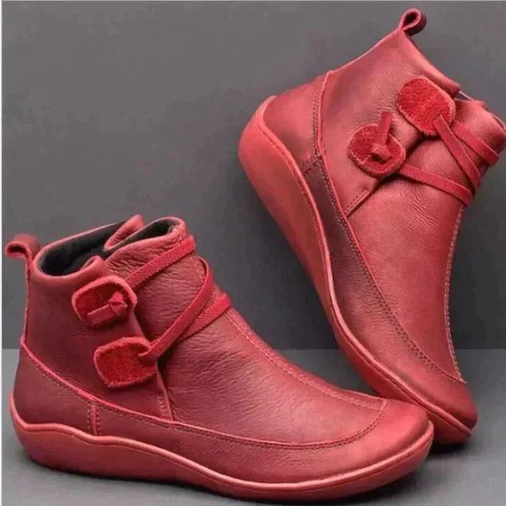 Botines planos rojos al tobillo mostrados en perspectivas opuestas, con costuras visibles, correas laterales y suelas a juego.