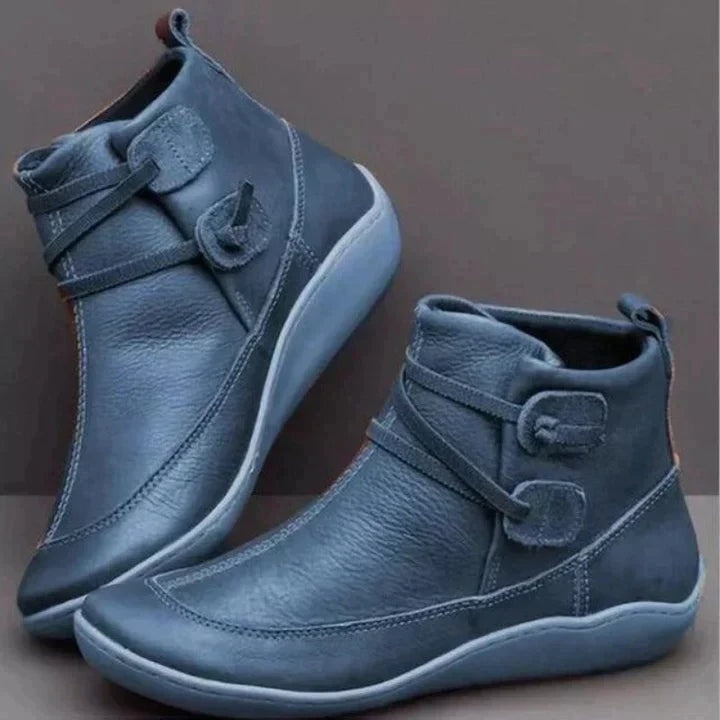 Botines planos azul oscuro al tobillo, vistos de lado y en diagonal, con dos correas laterales y suelas azul grisáceas.