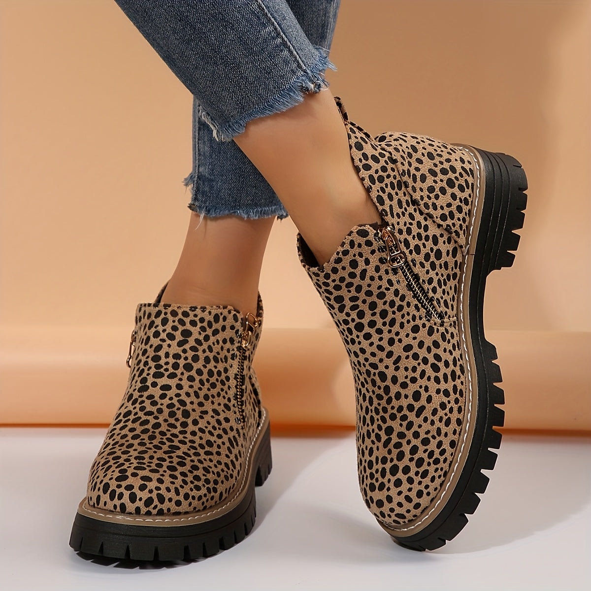 Botines planos de caña baja con estampado de leopardo, cremallera lateral y suela negra dentada, vistos en los pies con vaqueros.